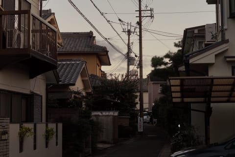 A quiet residential street at dusk lined with tiled-roof houses and tangled overhead power lines.