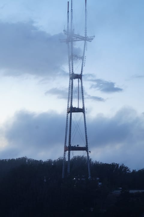 A tall steel broadcast tower rising into low cloud above a dark wooded ridge.