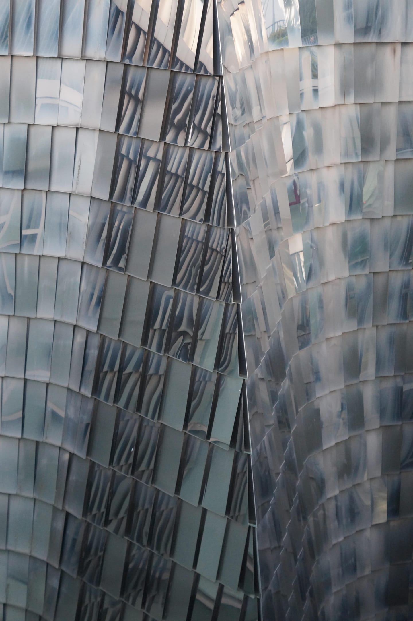 Abstract close-up of a curving, rippled metallic building facade in cool grey tones.