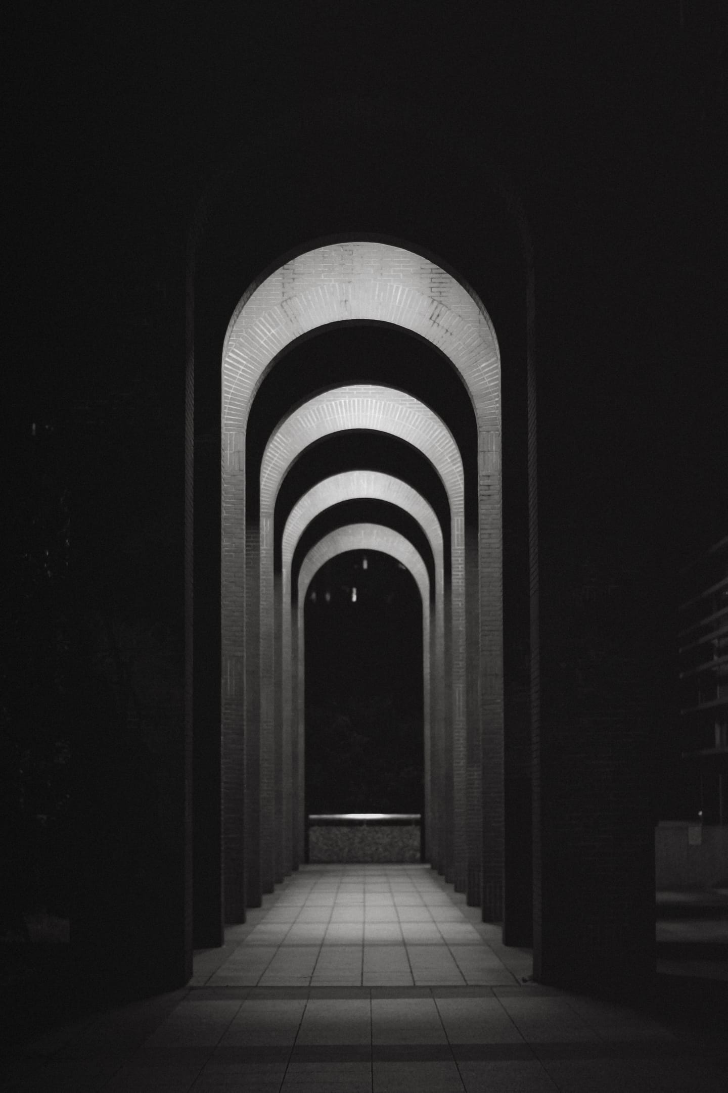 A black-and-white row of illuminated brick archways receding into darkness.