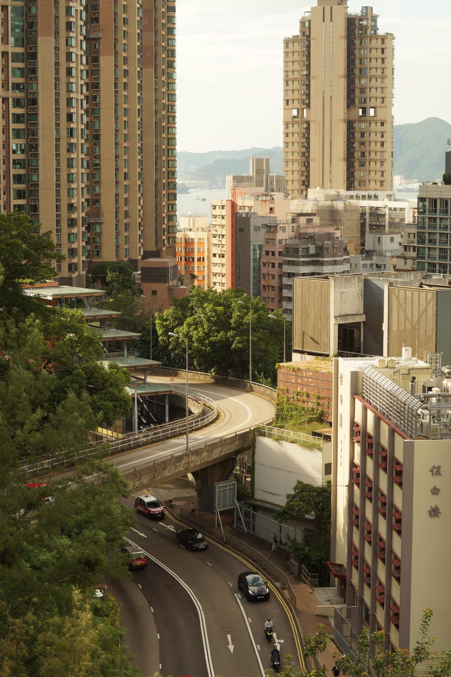 An elevated road curving between high-rise apartment towers, the sea visible in the distance.