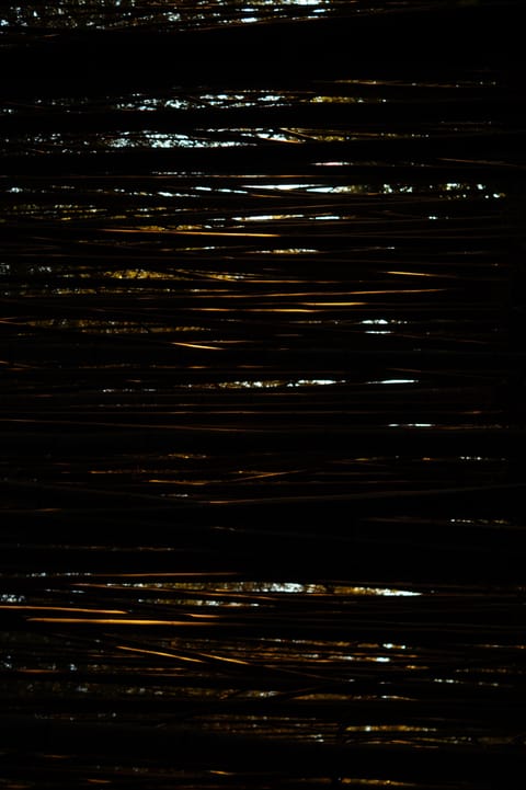 Threads of golden light reflecting across dark, rippled water at night.