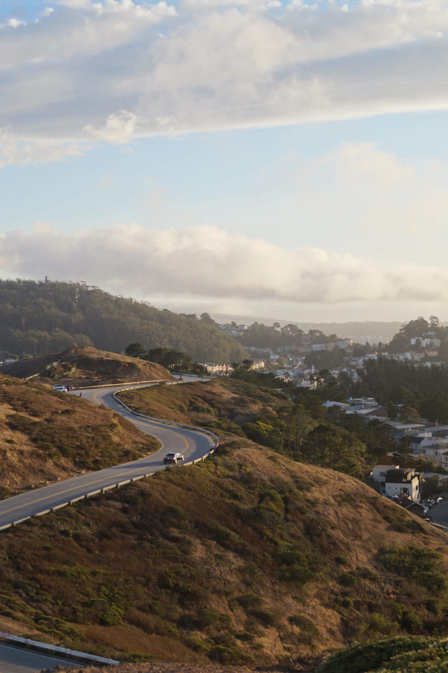 A winding road through golden coastal hills, with low fog and a town in the distance.