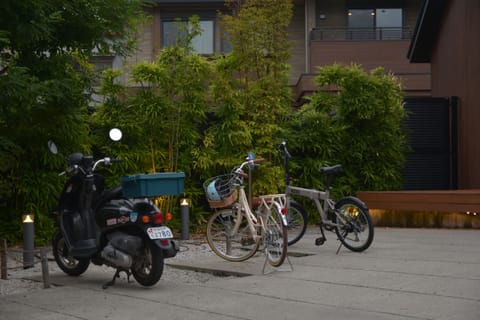 A moped and two bicycles parked beside bamboo outside a building at dusk.