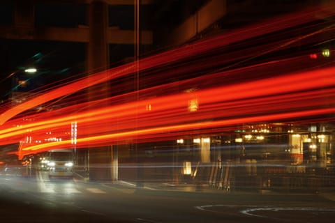 Long-exposure red light trails streaking under a highway overpass at night.