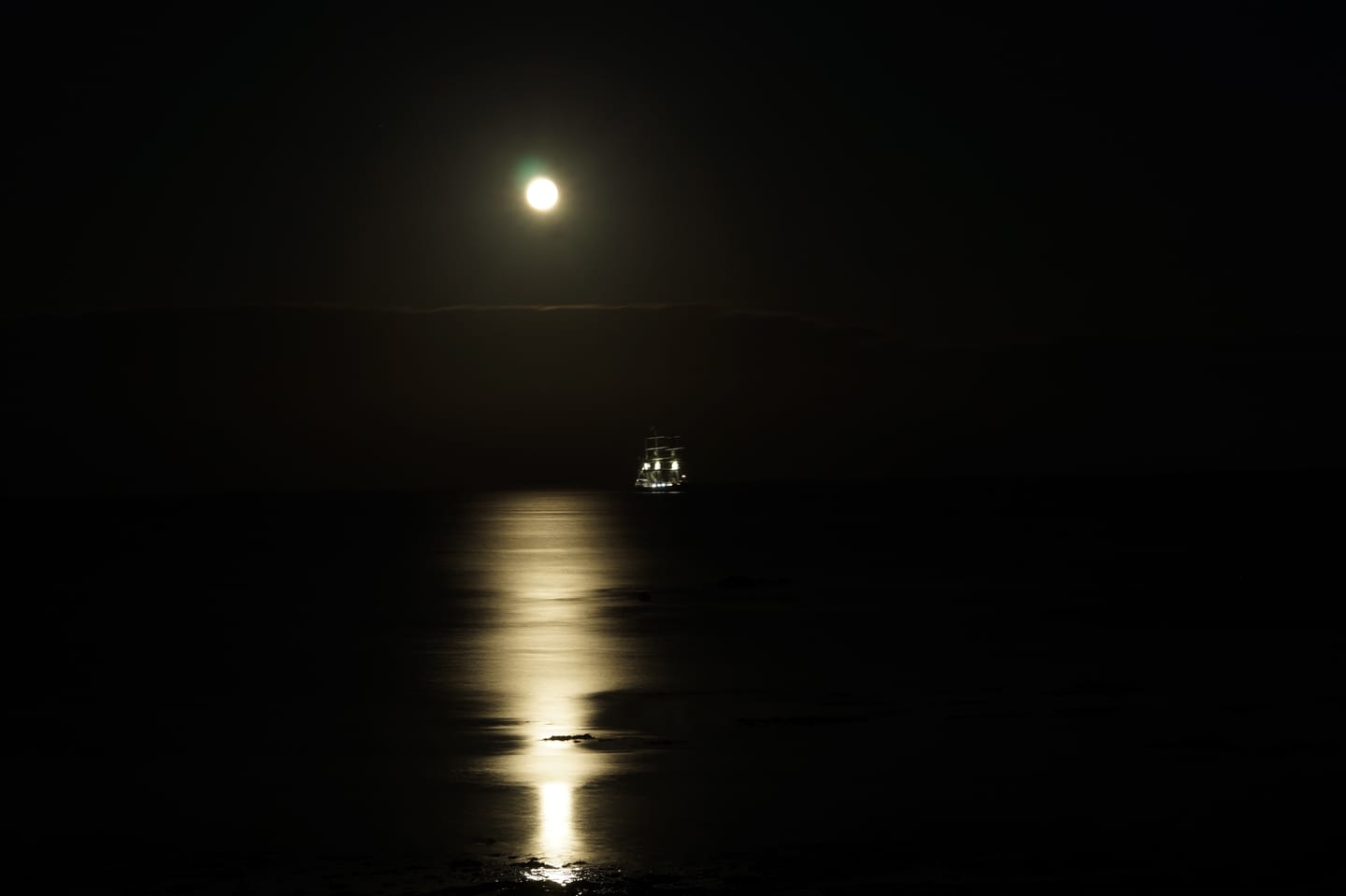 A full moon over the sea with a tall ship silhouetted and moonlight streaking across the water.