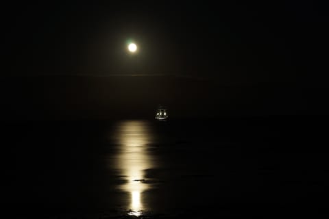 A full moon over the sea with a tall ship silhouetted and moonlight streaking across the water.