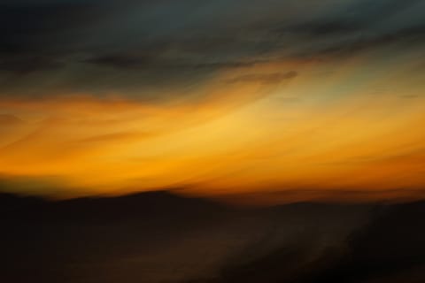 A vivid orange sunset sky over dark, motion-blurred hills.