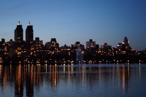 A city skyline at night, its lights reflected across a calm reservoir.