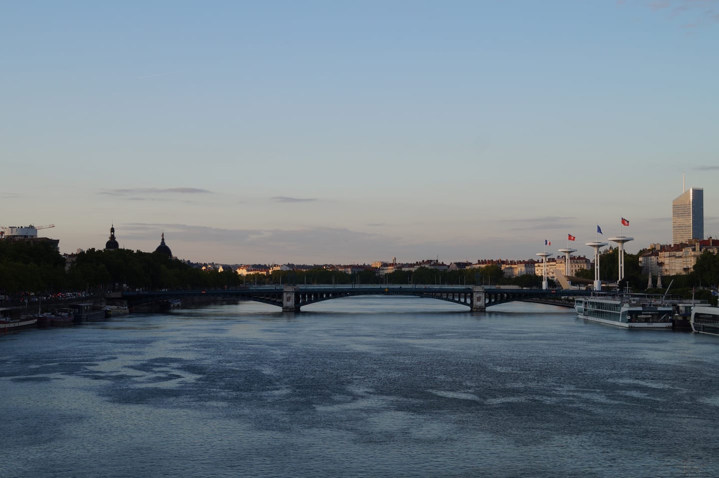 A bridge spanning a calm river at dusk, with a city skyline along the far bank.