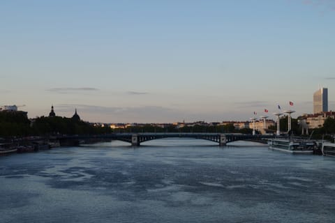 A bridge spanning a calm river at dusk, with a city skyline along the far bank.